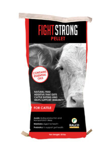 A 50-lb bag labeled "FIGHT STRONG PELLET" for cattle, showing two cows. The bag highlights essential oils, immune support, and gut health benefits. Brand: Ralco. Text indicates it assists with digestion and stress.