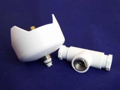 Two white plastic plumbing fittings with metal threads rest on a blue surface; one part is bowl-shaped and upright, the other is a T-shaped connector lying beside it.