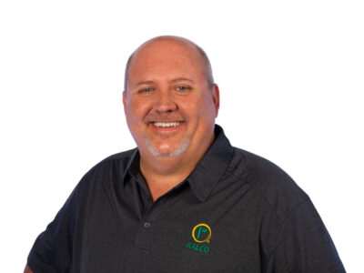 Smiling middle-aged man with short hair and a goatee, wearing a dark polo shirt with a “RALCO” logo, standing against a plain white background.