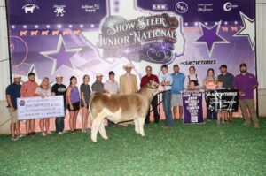 A group of people pose with a steer and awards at the Show Steer Junior Nationals. Signs, banners, a large check, and trophies are displayed. The background features logos, stars, and purple lighting.