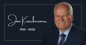 Memorial image with the text "Jon Knochenmus 1955 - 2022" next to a smiling older man in a suit and tie, set against a dark background with a simple border.