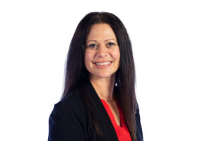 Woman with long dark hair wearing a black blazer and red top, smiling at the camera against a plain white background.