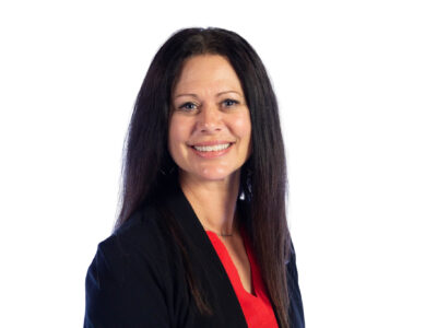 Woman with long dark hair wearing a black blazer and red top, smiling at the camera against a plain white background.