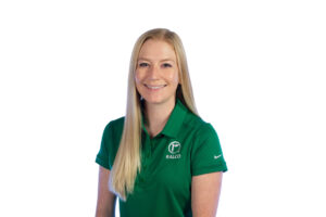 A woman with long blond hair smiles at the camera. She is wearing a green polo shirt with the Ralco logo and a Nike logo on the sleeve, standing against a plain white background.