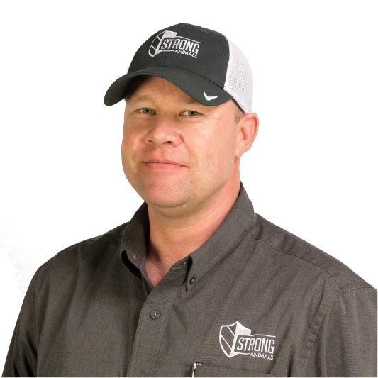 A man wearing a black and white "Strong Animals" cap and a gray "Strong Animals" collared shirt stands smiling slightly against a plain white background.