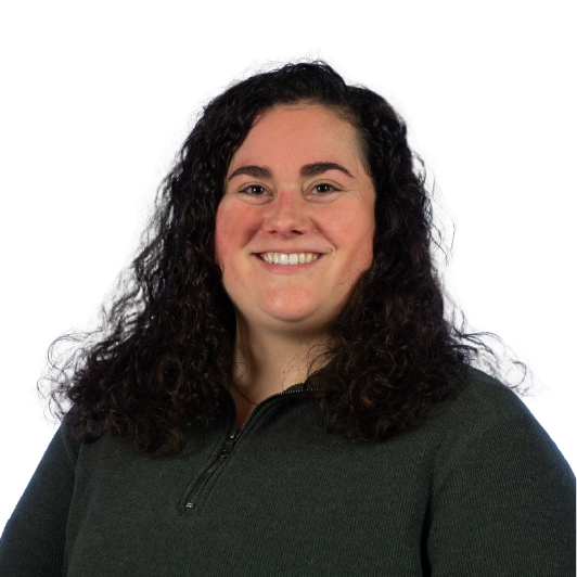 A woman with long, curly dark hair smiles at the camera. She is wearing a dark green zip-up sweater and is posed against a plain white background.