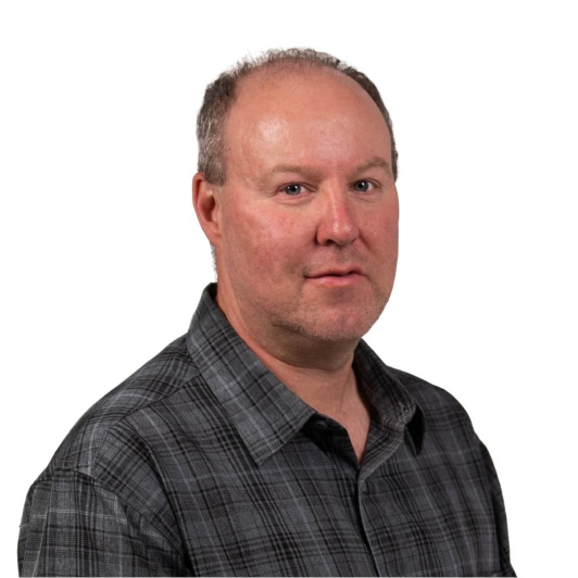 A middle-aged man with short, thinning hair wearing a gray plaid shirt poses against a plain white background.