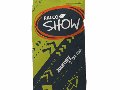 A green and black livestock feed bag labeled "Full Bloom" with orange and white accents, featuring geometric arrow designs and the phrase "Journey to the Ring" on the front.