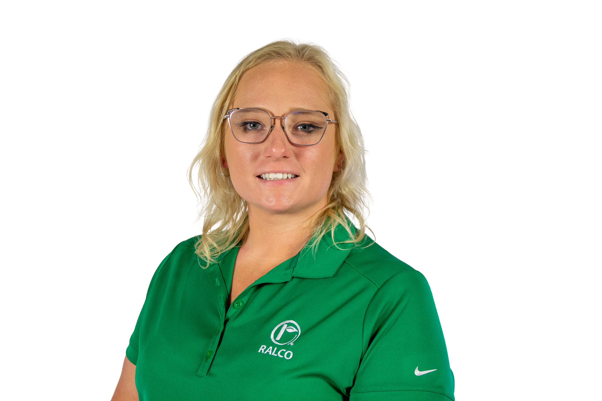 A woman with blonde hair and glasses wearing a green RALCO-branded polo shirt stands against a plain white background, smiling slightly at the camera.